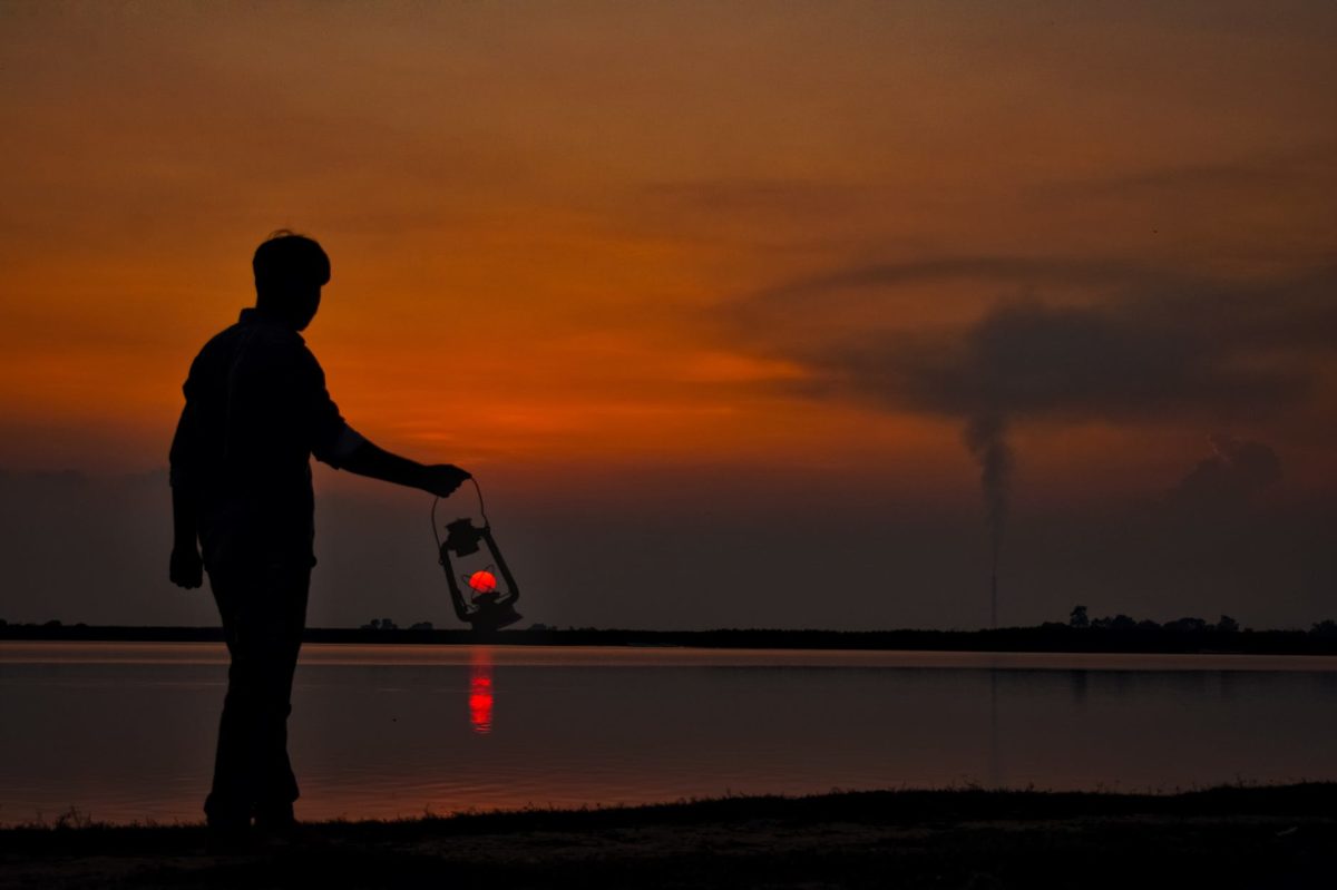 silhouette of man with oil lamp on shore at sunset